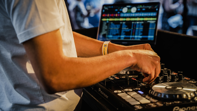 DJ steht am DJ-Pult und dreht an Knöpfen.